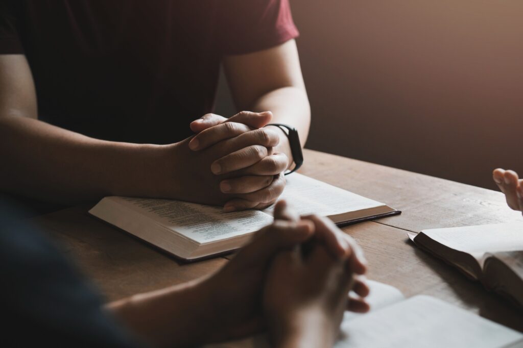 A group of Christians sit together and pray around a wooden table